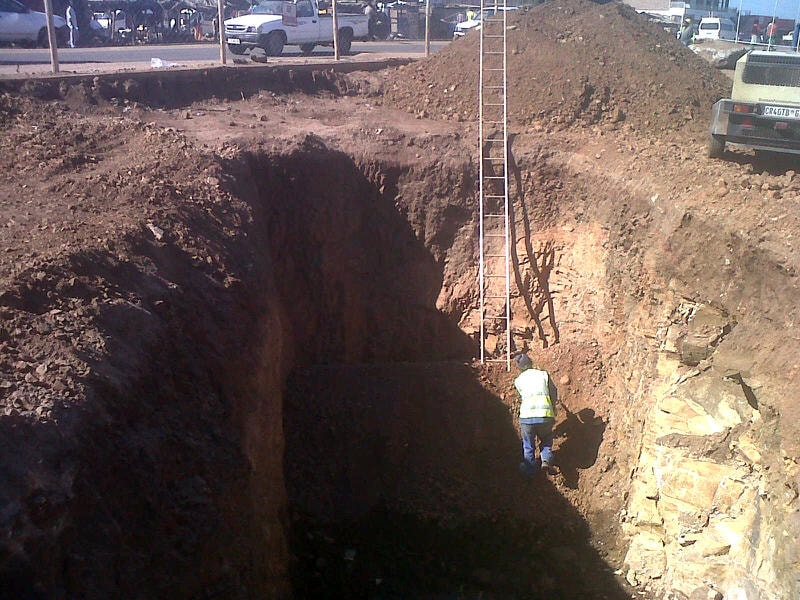 Worker descending into deep excavation pit